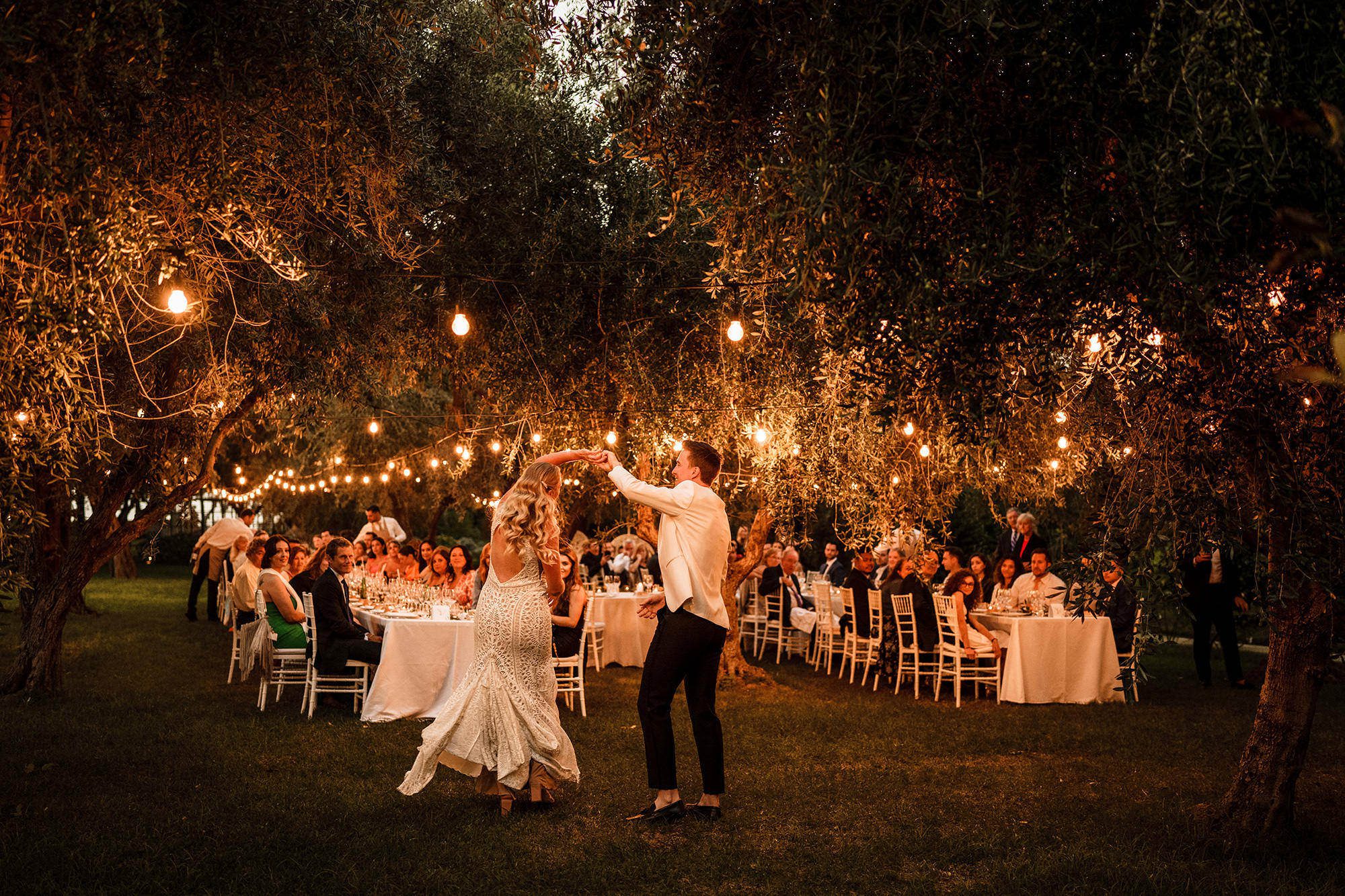 Couple dancing outside during wedding reception under warm evening lights